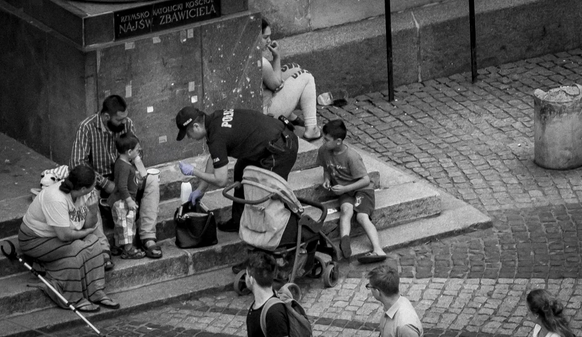 Police officer kneeling to show something to a small child beside a stroller on the steps
